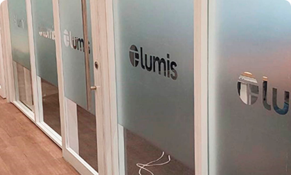 Adesivação em película jateada aplicada em divisórias e portas de vidro de um escritório, exibindo o logotipo da marca 'lumis'.